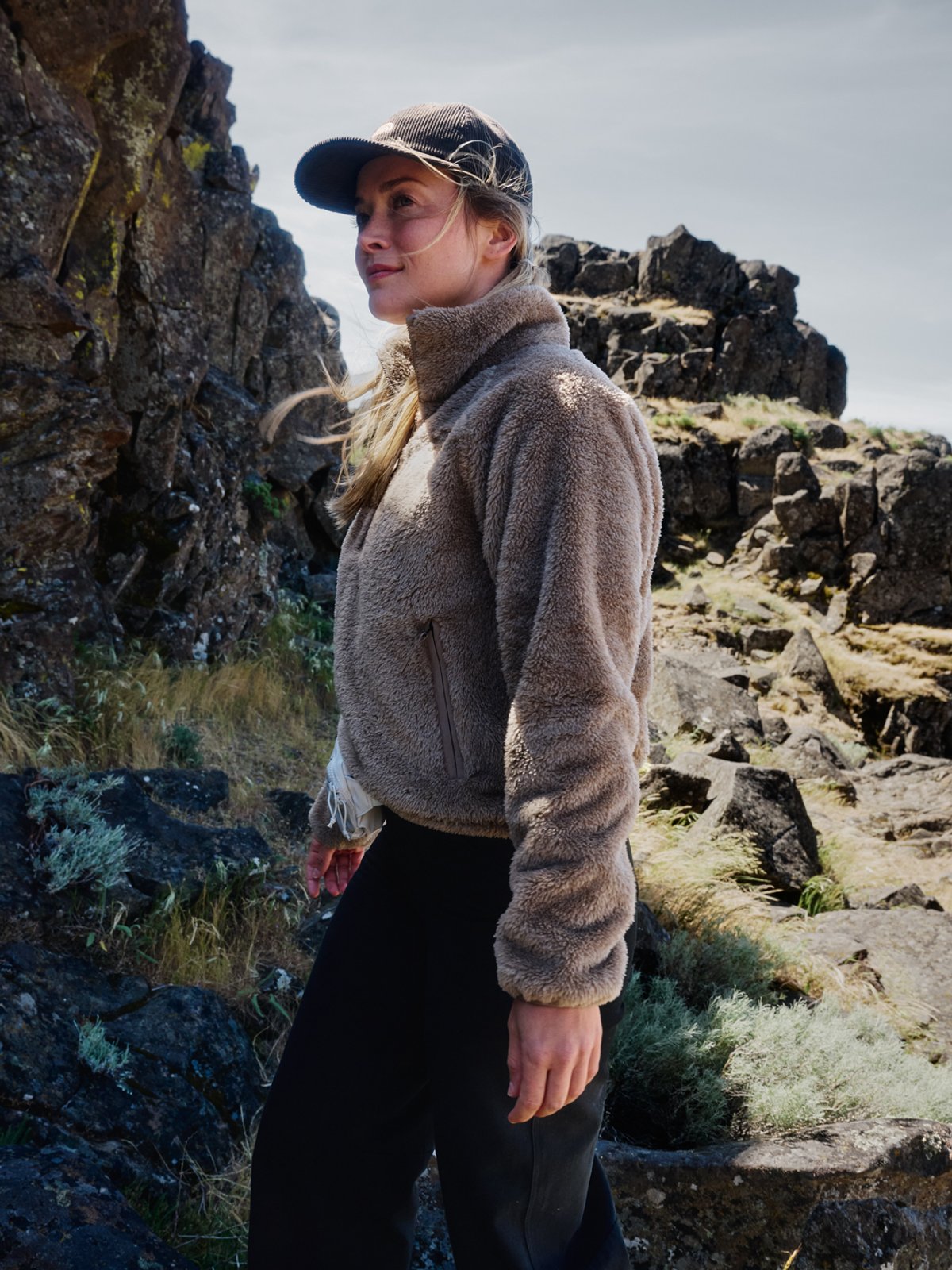 A woman stands against a rocky landscape, wearing The North Face fleece.