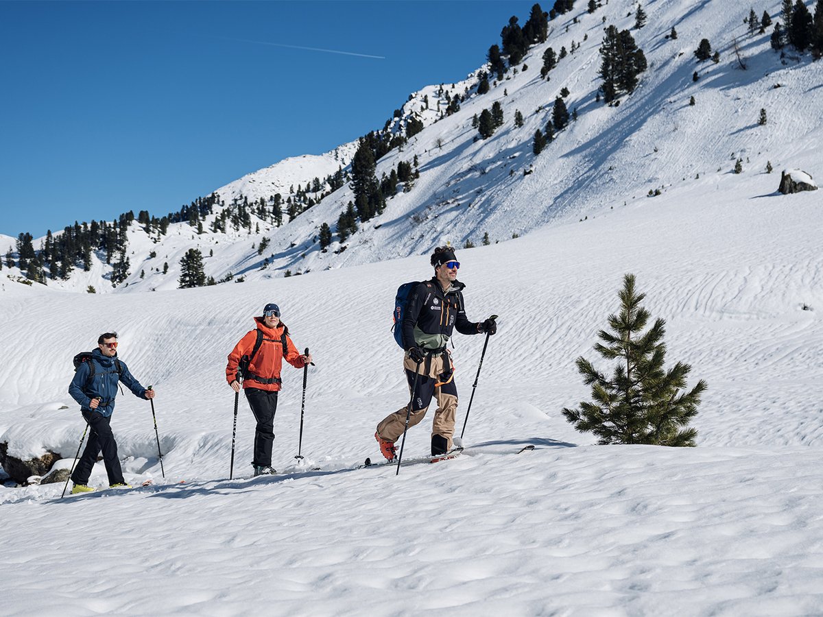 Three skiers touring across an open snow slope.