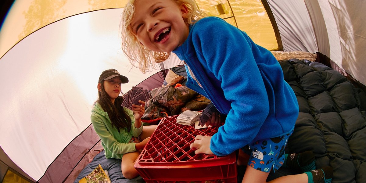 Two kiddos play cards inside their camping tent.