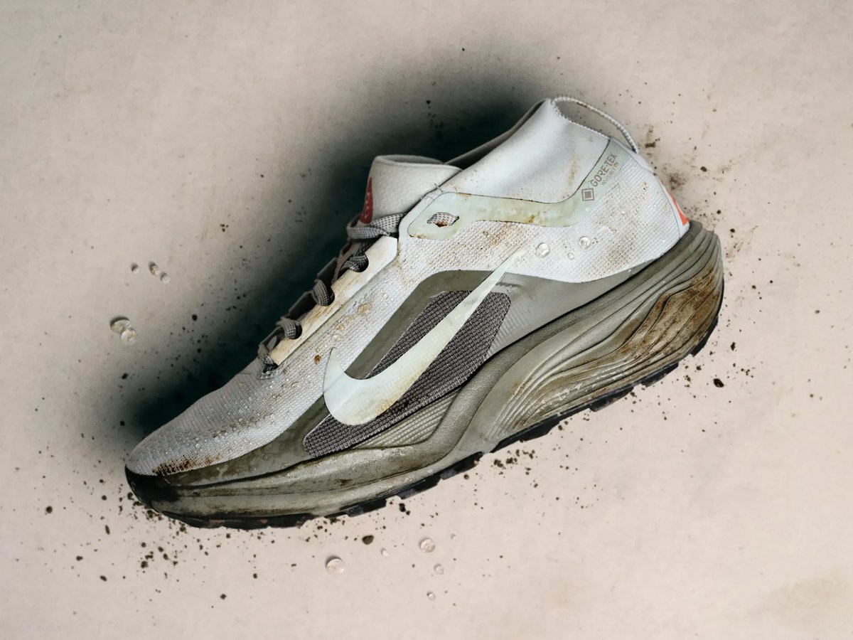 Mud-caked Nike Pegasus GTX trail running shoe with chunky midsole, surrounded by dirt splatter and water droplets on a light surface.
