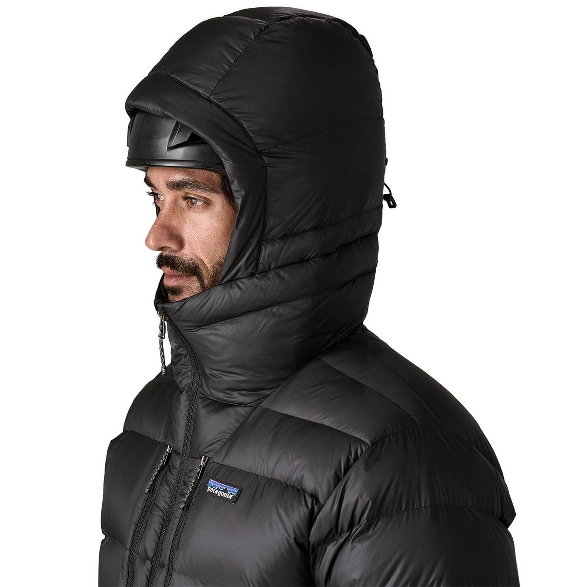 Person withwearing climbing helmet with Fitz Roy jacket hood pulled up and fully zipped.