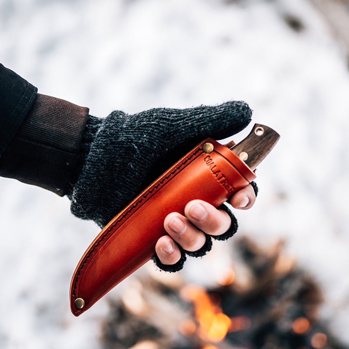 Person wearing gloves holding the Coalatree Haswell Knife in winter over a campfire