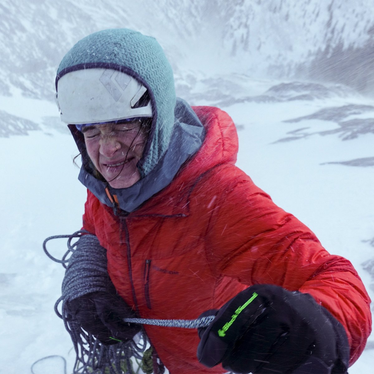 Climber in a red Capilene baselayer top ascending a snowy mountain slope, ice axe in hand.