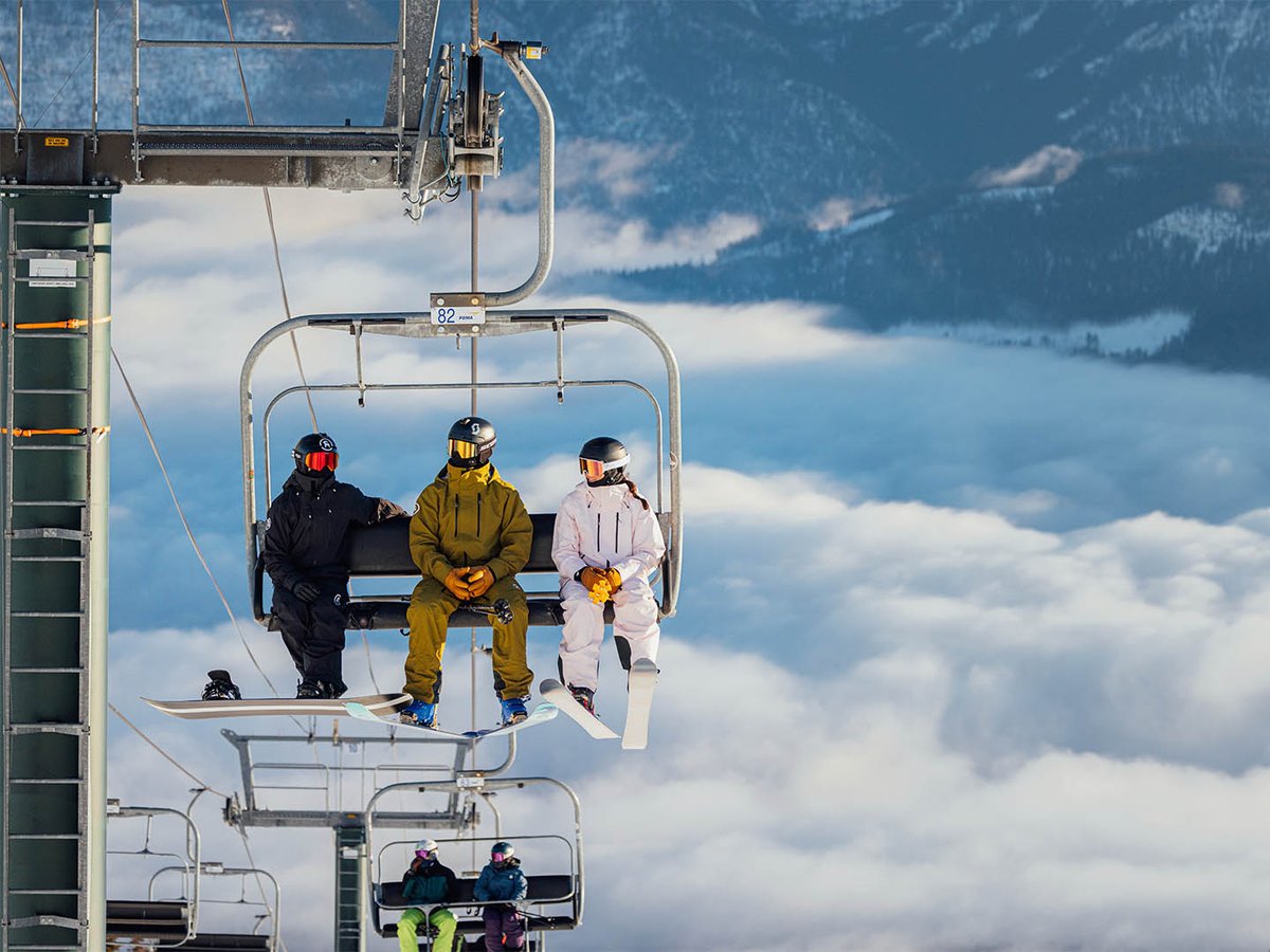 Skier walking holding skis and poled on rocly snow mountain top with view from below.