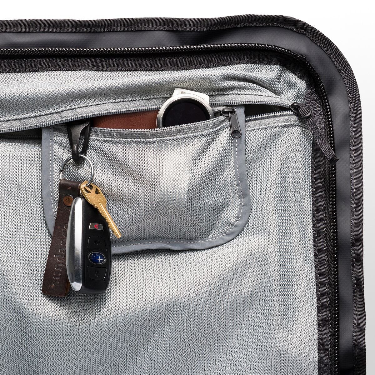 Interior pocket of a duffel bag with keys, wallet, and smart watch organized in mesh compartments.