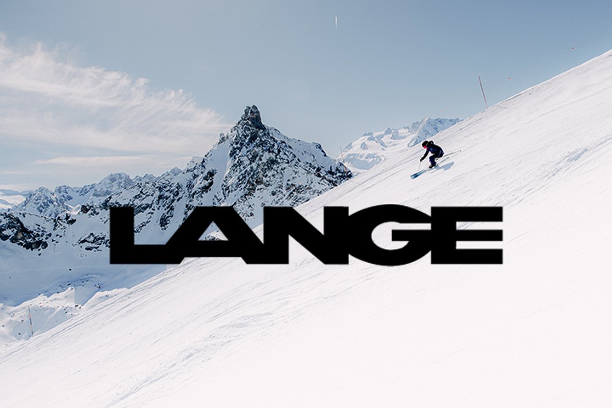 Skier descending steep alpine slope with Lange logo over snowy mountain landscape