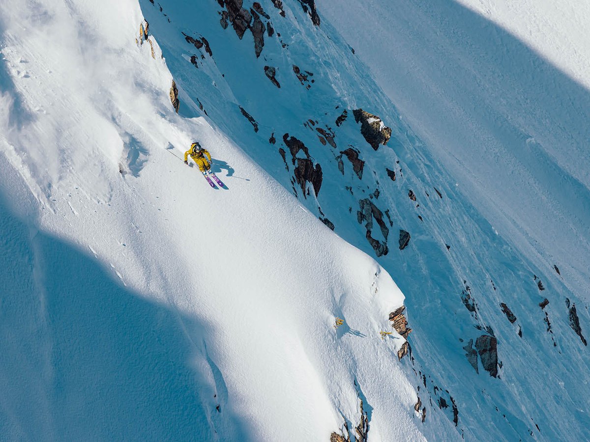 Skier riding down steep mountain ridge.