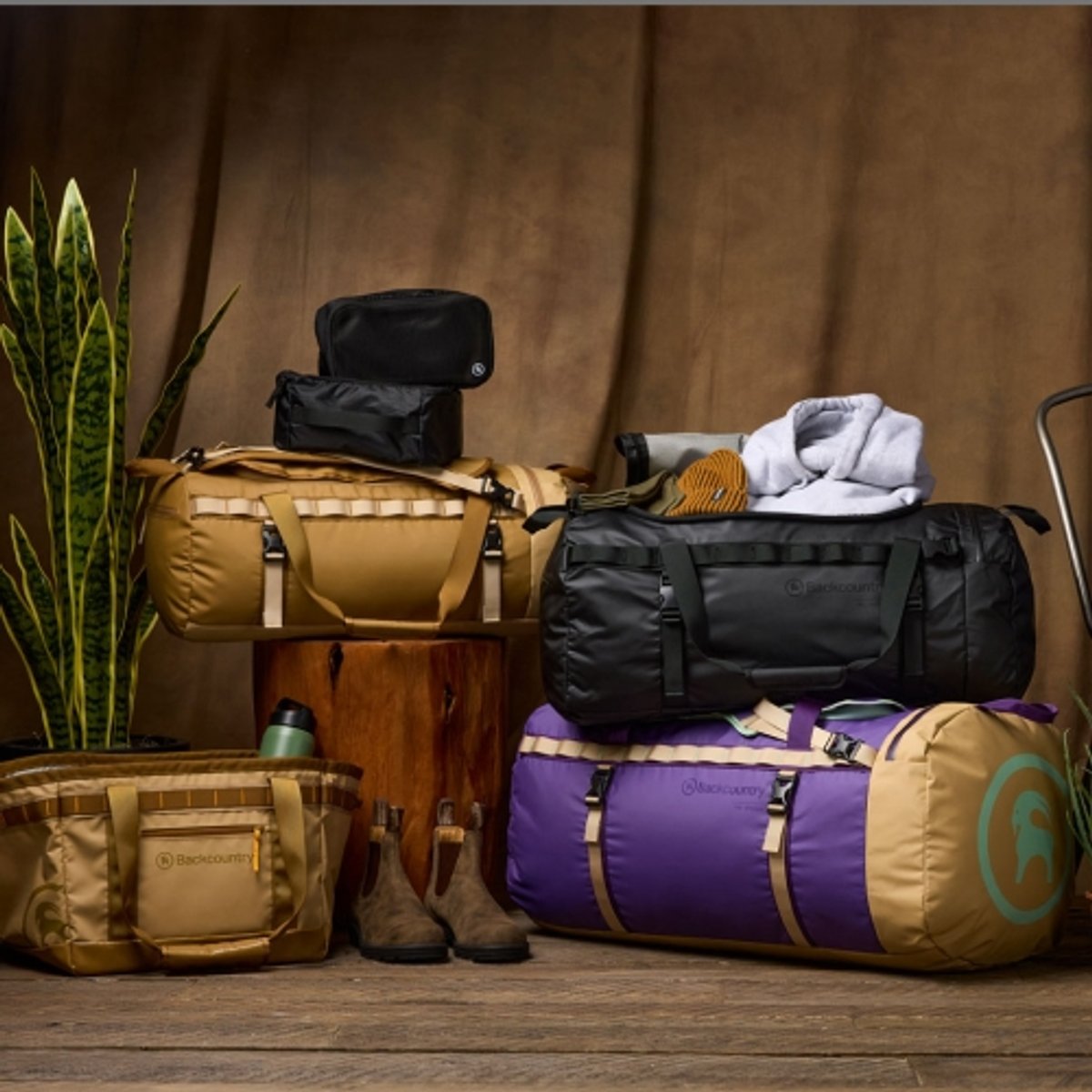 Several duffel bags and backpacks stacked on top of each other with a wooden background. 