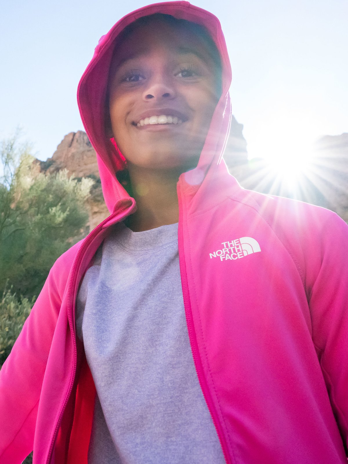 A smiling child wearing a bright pink The North Face fleece hoodie over a gray t-shirt.