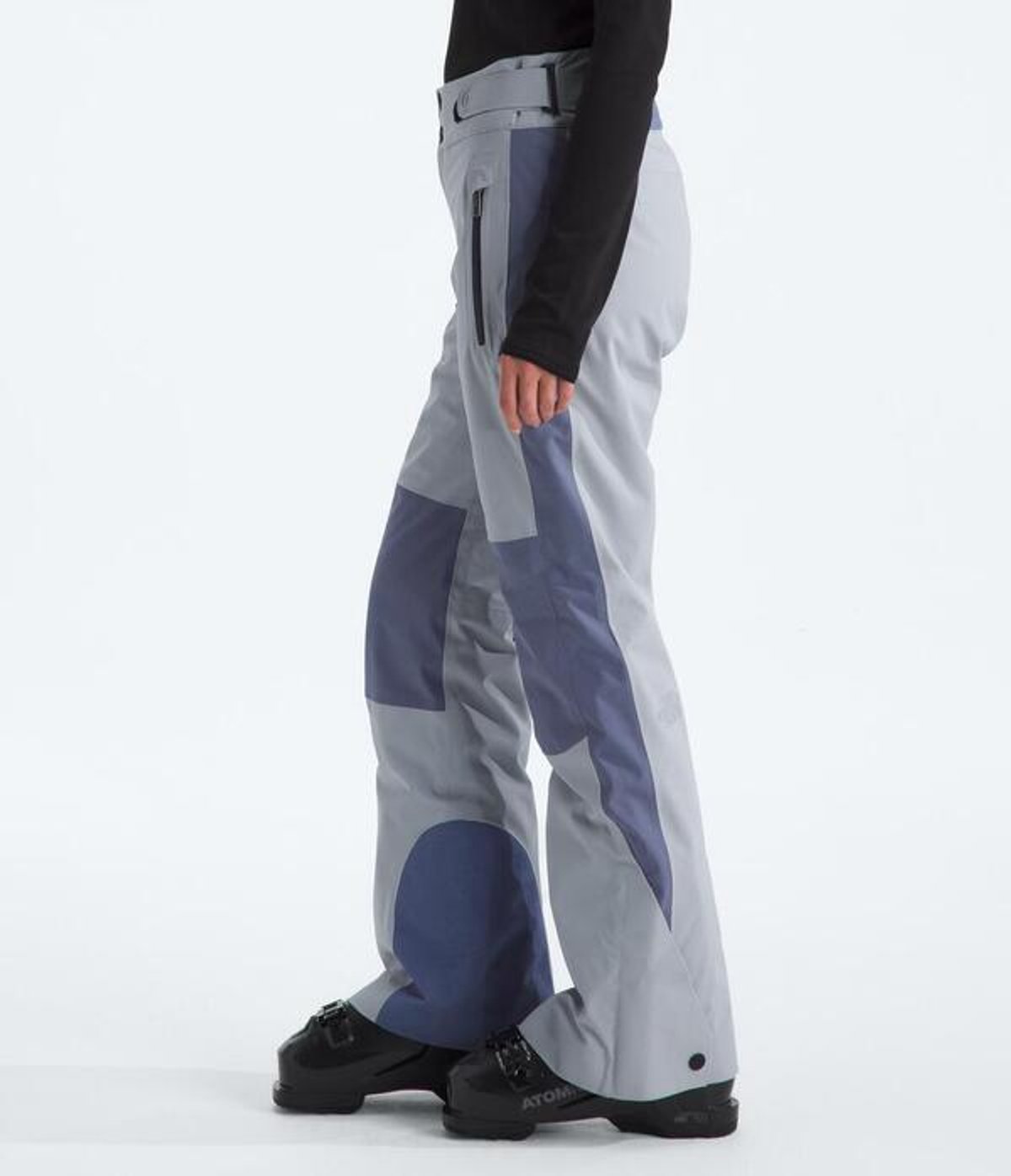 Person wearing snow pants and ski boots facing to the side.