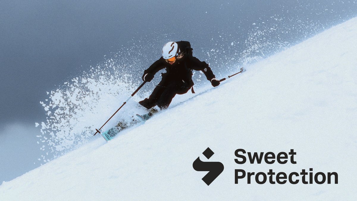 A skier in black winter gear and a white helmet descends a snowy slope, spraying powder, with the Sweet Protection brand logo displayed in the lower right corner.