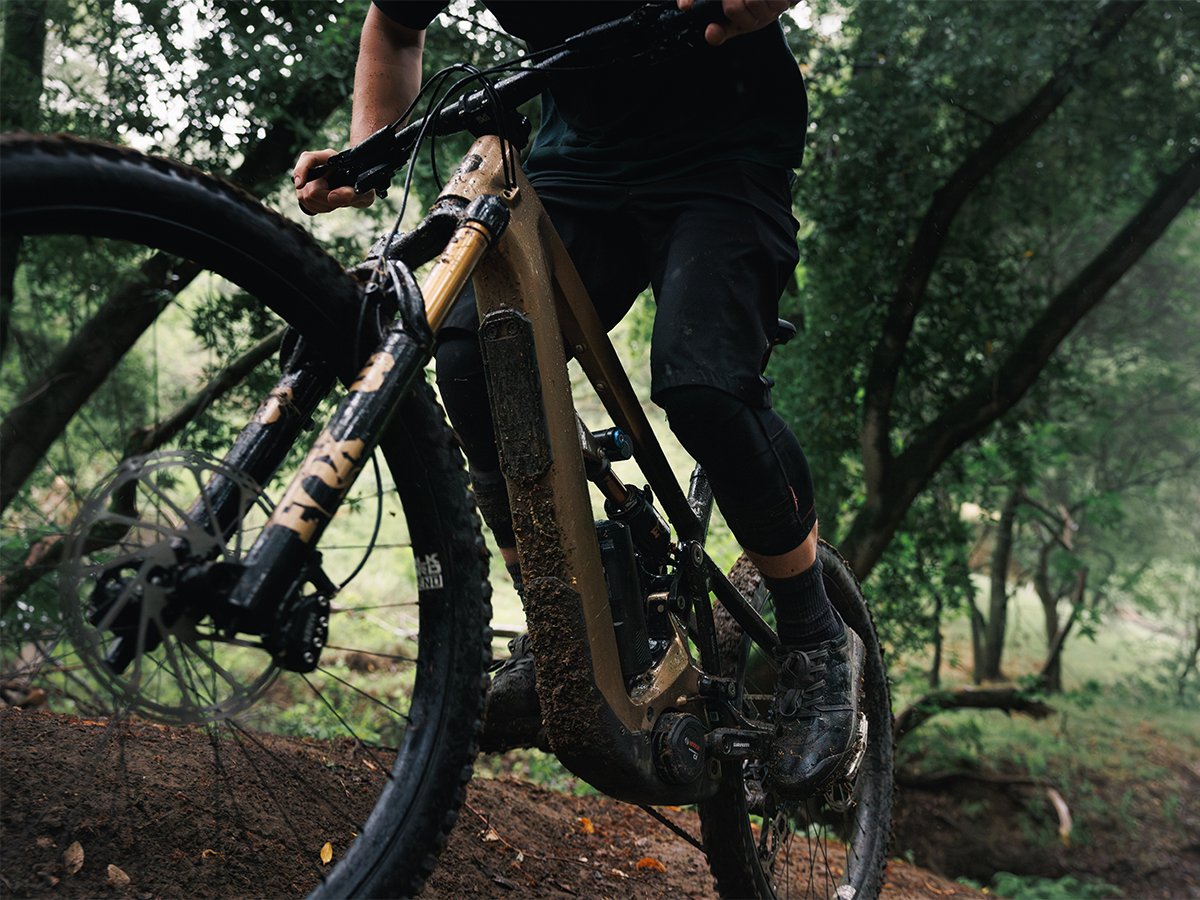 Close-up of rider pedaling full-suspension eMTB showing drivetrain and knobby tire on forested dirt trail