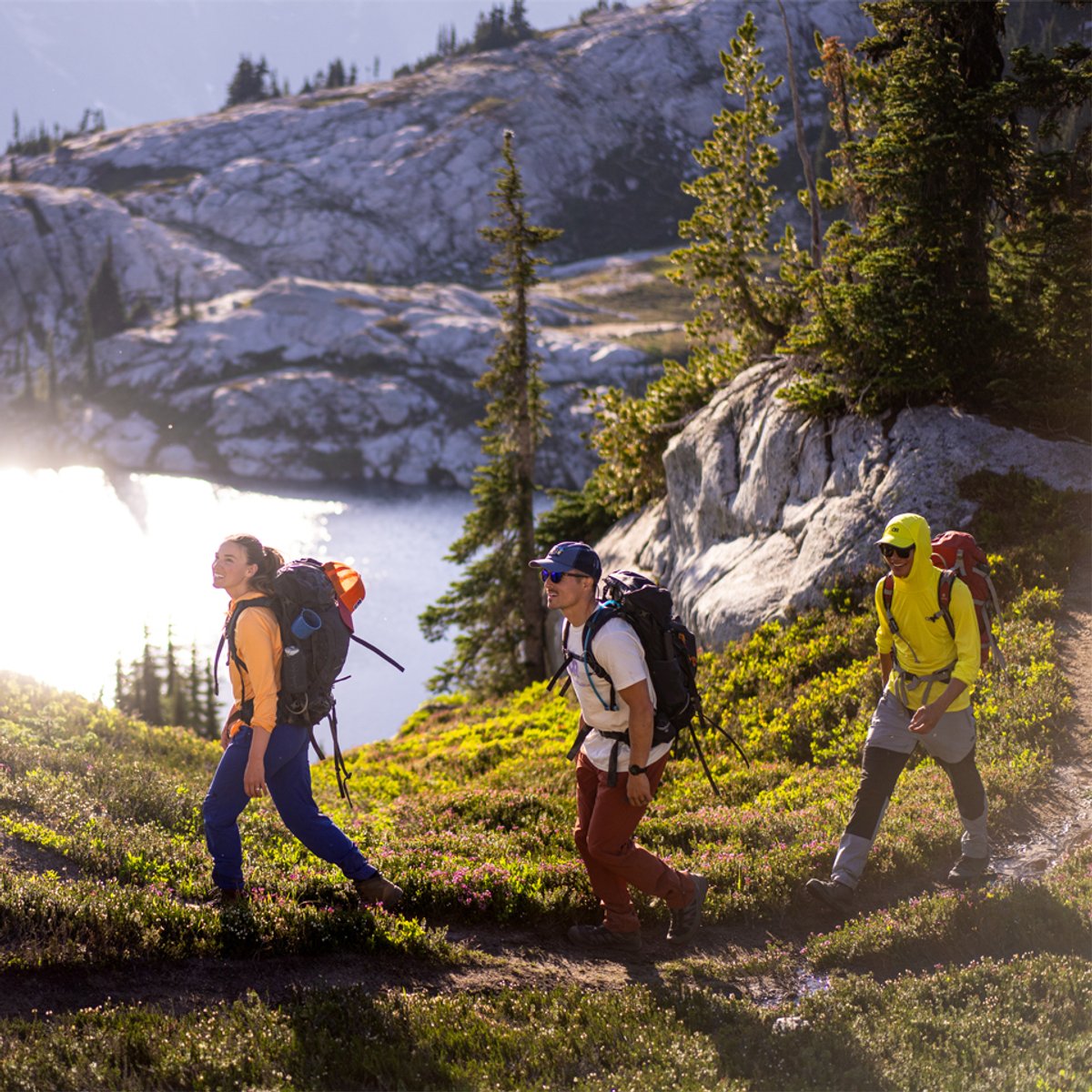 A group of three people walks along an alpine trail, wearing Ferrosi gear.
