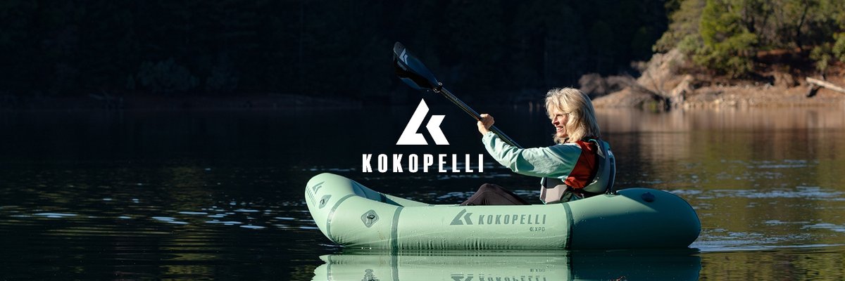 A woman paddles a green inflatable Kokopelli kayak on a calm lake, with the brand's logo in the center.