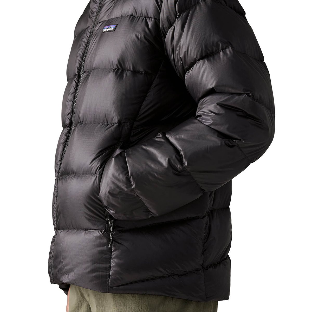 Person with hands inside black Fitz Roy jacket handwarmer pockets.