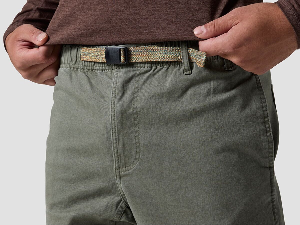 Close-up of a person wearing green pants with a woven belt, hand resting near the waistband.