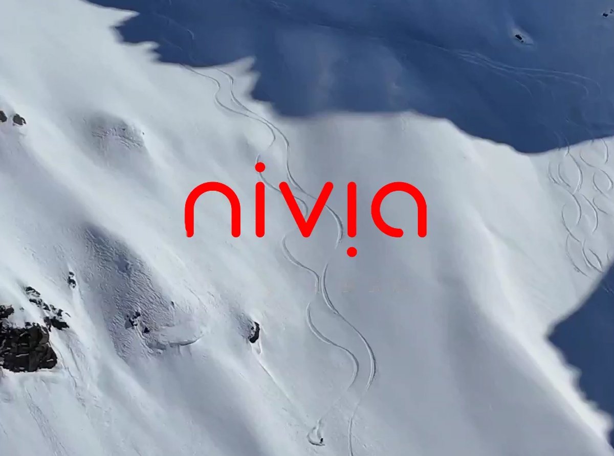 Red Nivia logo overlayed on steep mountain slope with s lines carved into the snow and a skier descending.