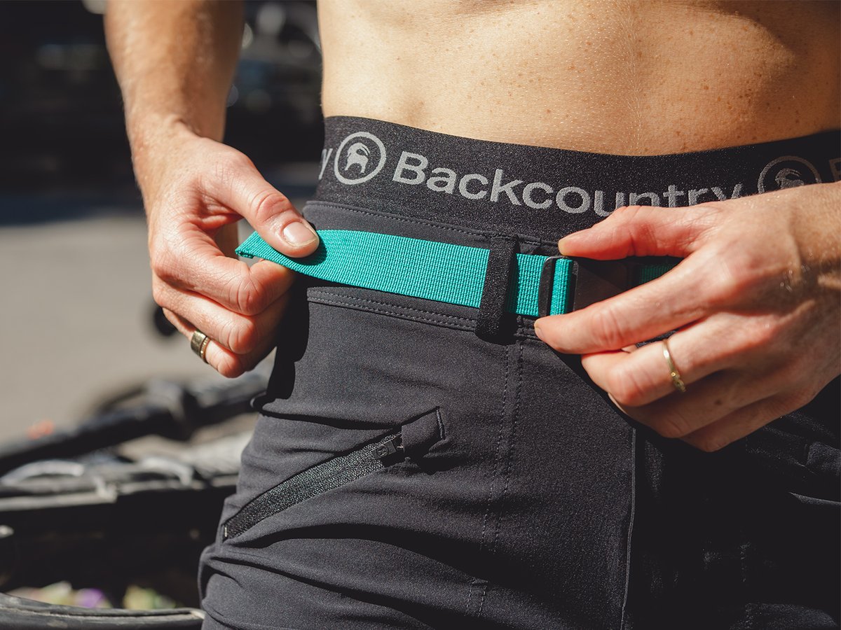 Person tightening integrated belt webbing on Slickrock shorts.