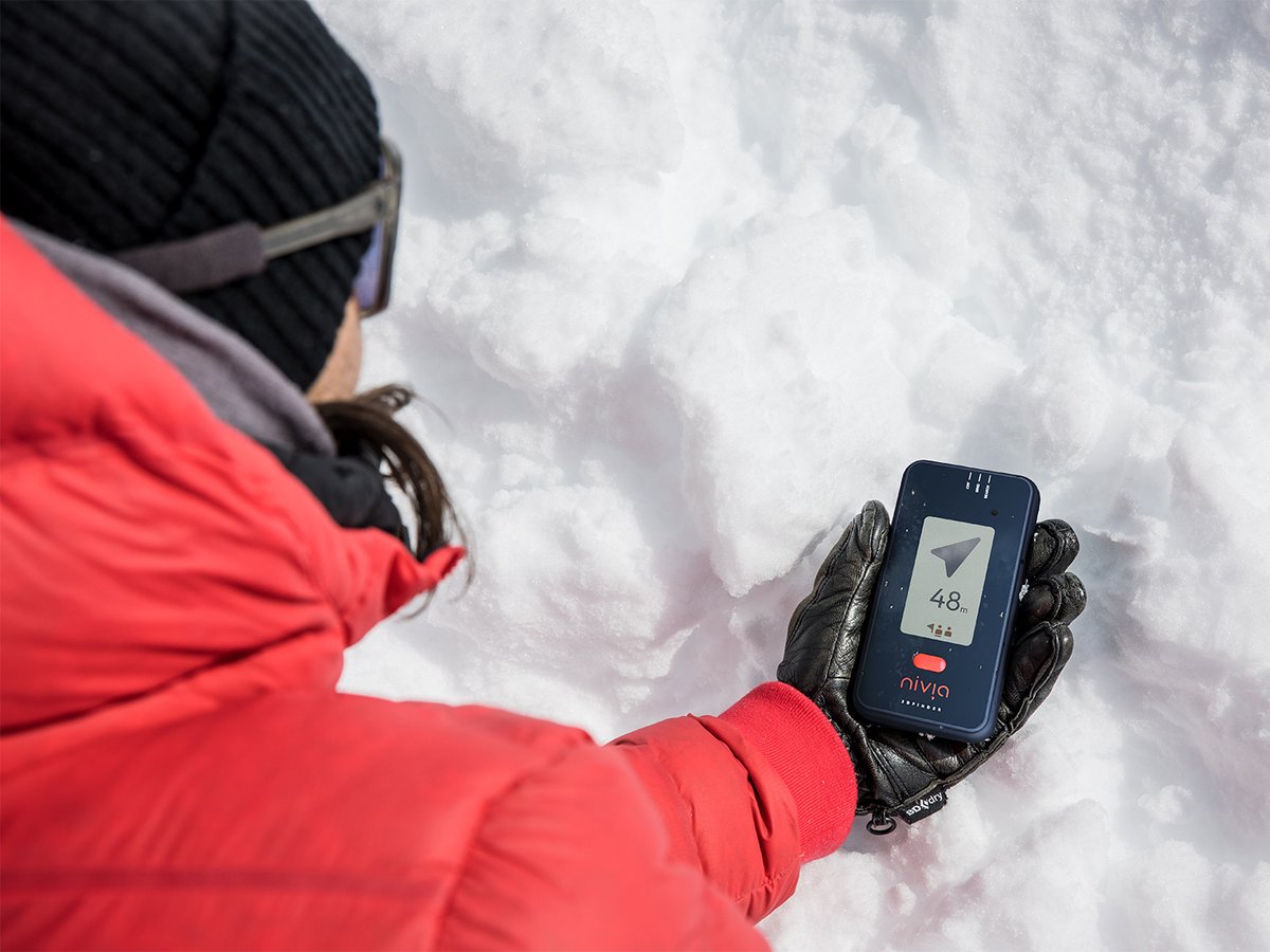 Gloved hand holding a Nivia 3D Finder, red control button visible below the screen.