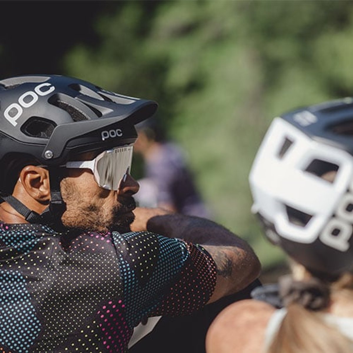 two people lean on a truck tailgate, wearing POC mountain bike helmets