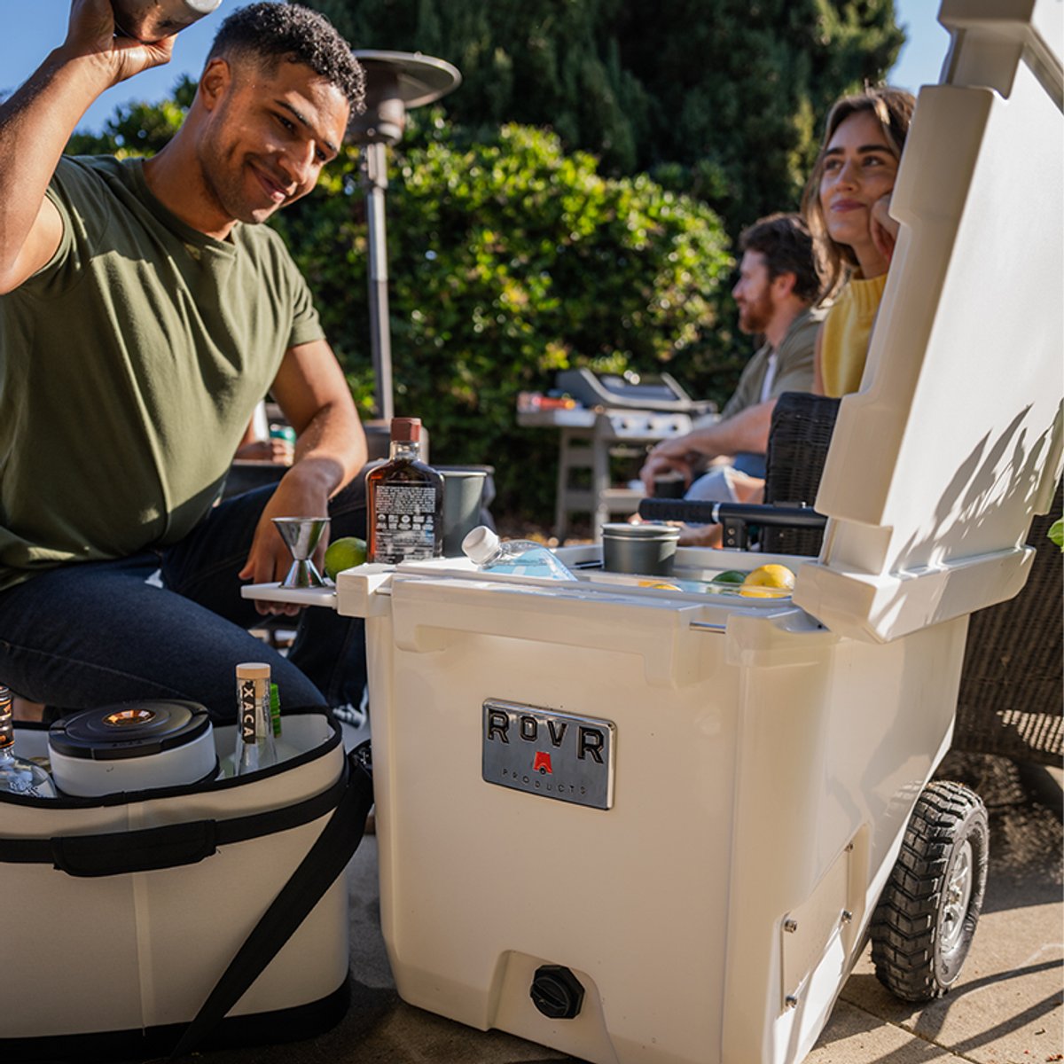 Open RovR RollR cooler on a patio used as a drink station while friends prepare cocktails outdoors.