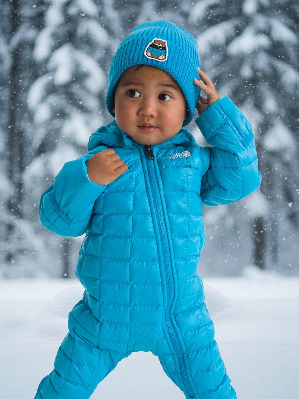 An infant wearing a quilted zip-up bunting and matching knit hat.