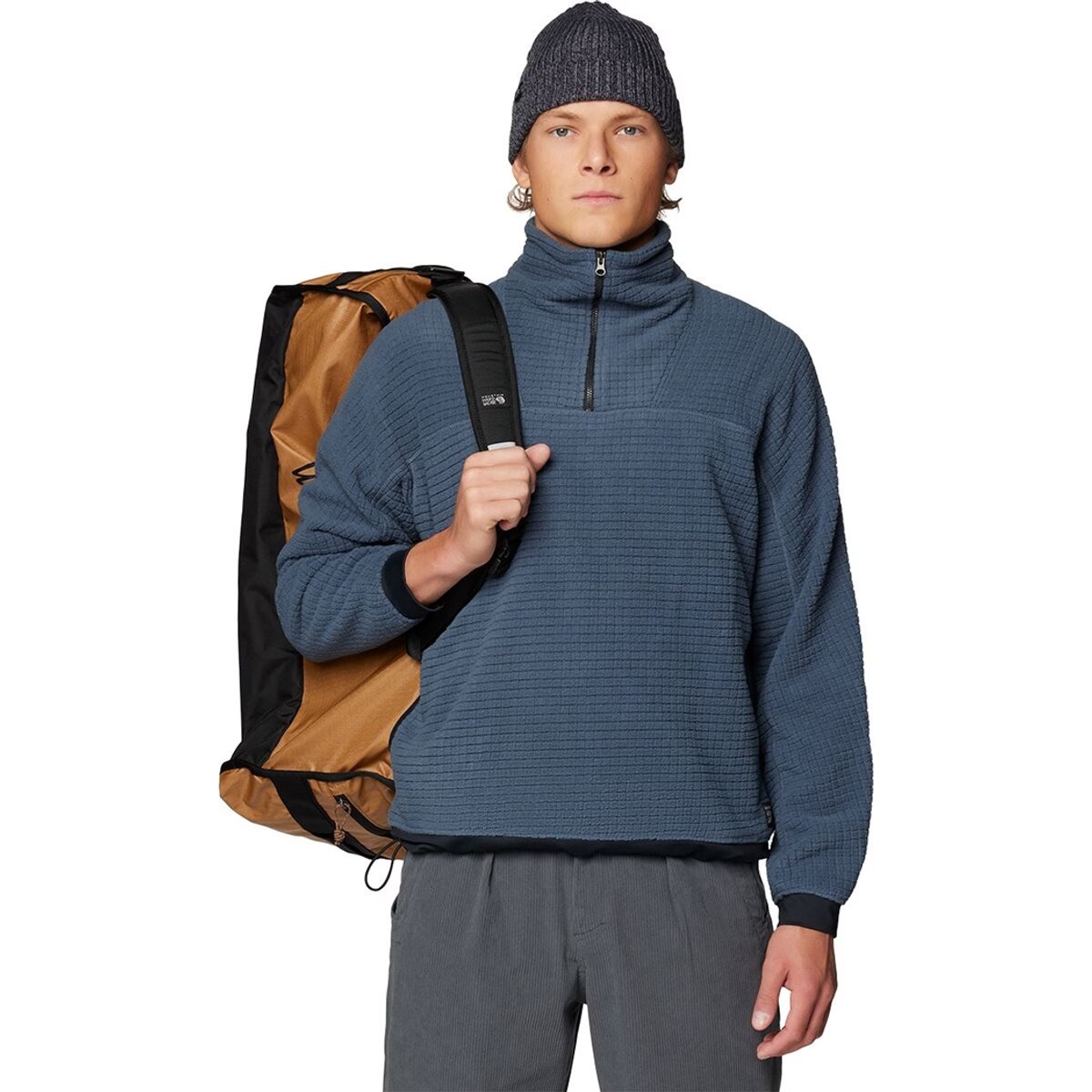A man wears the Summit Grid Big Grid 1/2 Zip Pullover, holding a backpack over one shoulder. 
