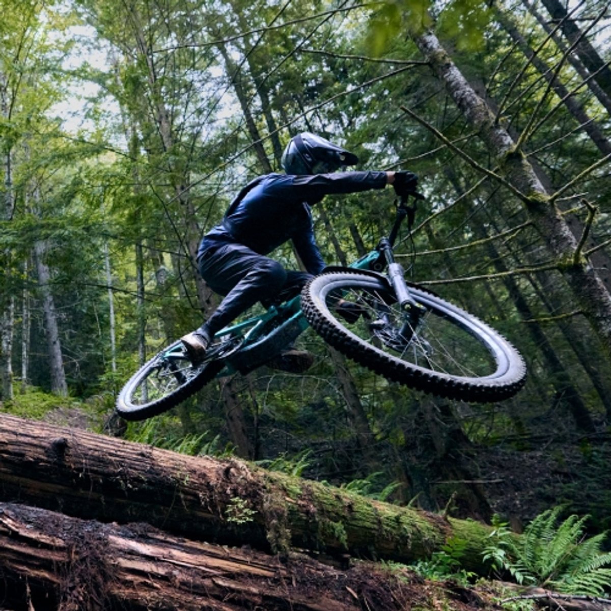 Mountain biker performs an aerial maneuver while riding down a forested trail. 