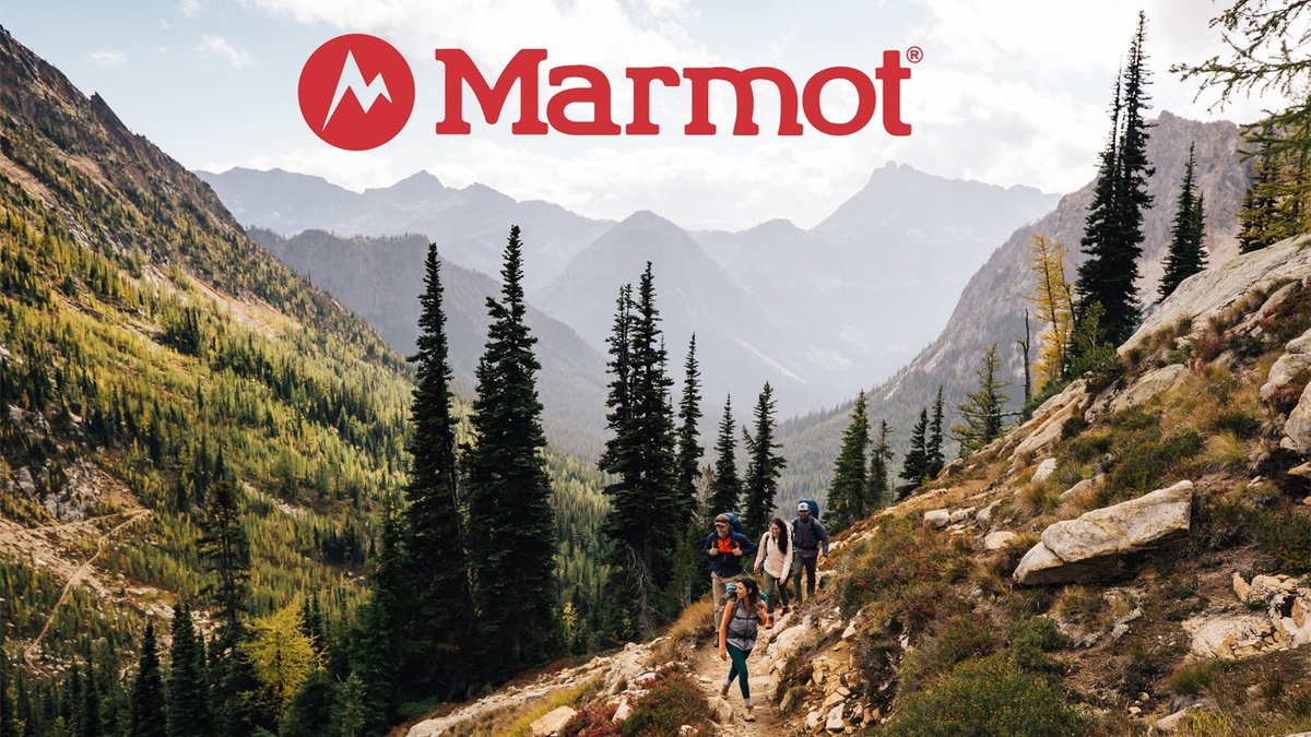 A group of hikers walking down a mountain trail with a vast valley and evergreen trees in the background; the red Marmot logo is at the top.