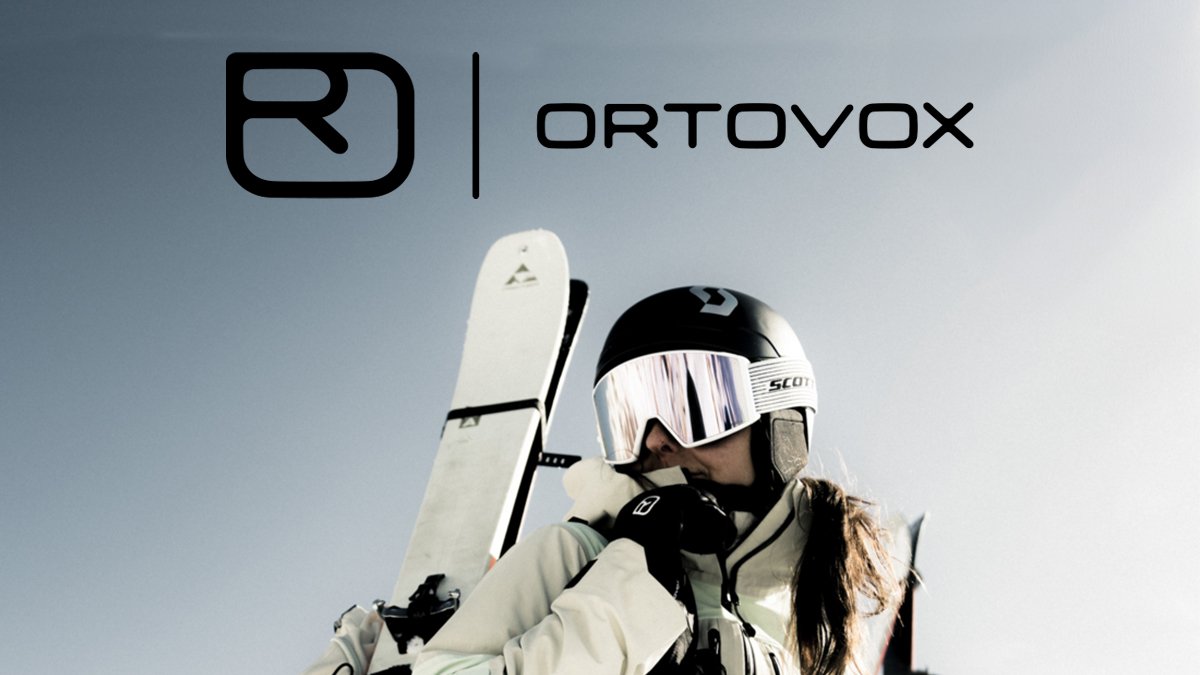 A skier in winter gear holds a white ski while wearing a black and white helmet and mirrored goggles against a blue sky background, with the Ortovox brand logo displayed above.