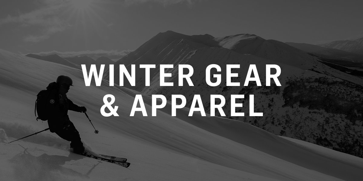 A skier carves down a wide, open snowfield with mountain ridges rising in the background. Text reads "Winter Gear & Apparel.