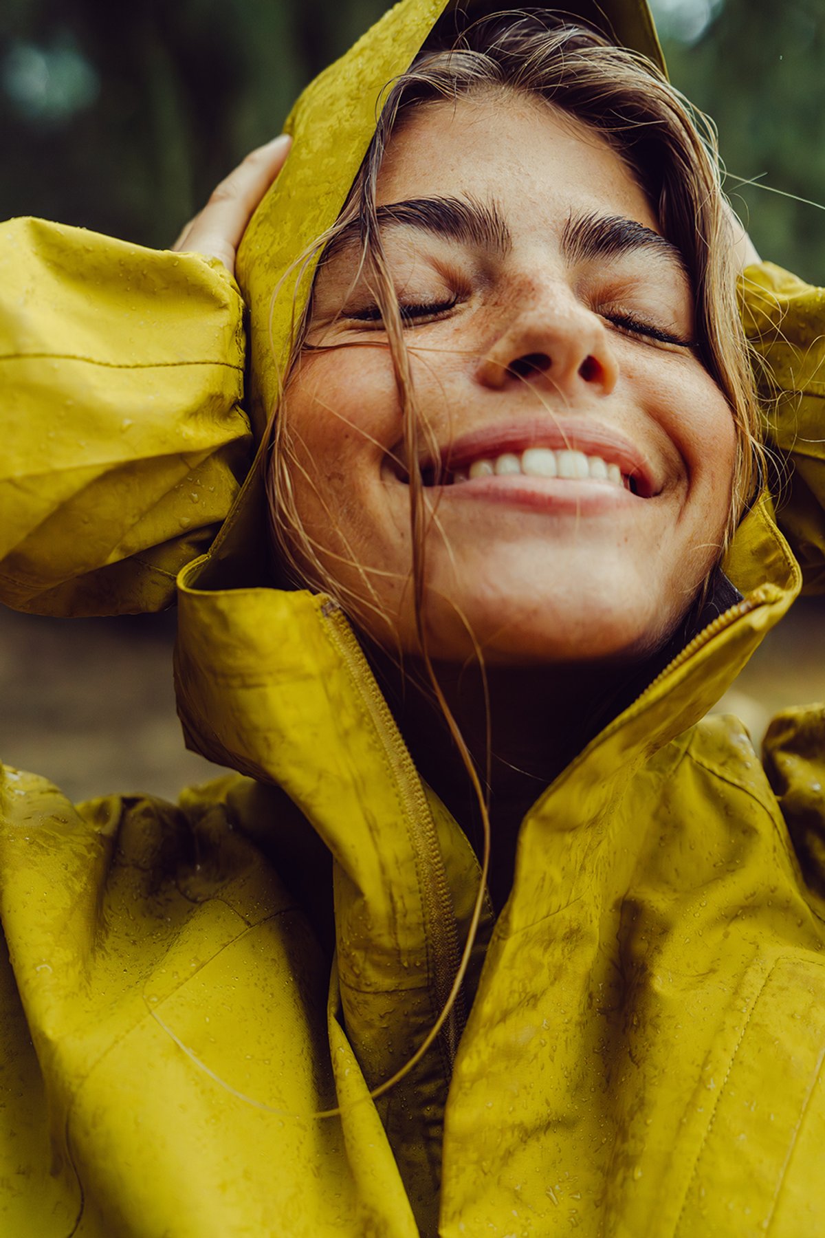 Woman wearing yellow hooded waterproof rain jacket with wet face and hair in rainy tropical forest conditions