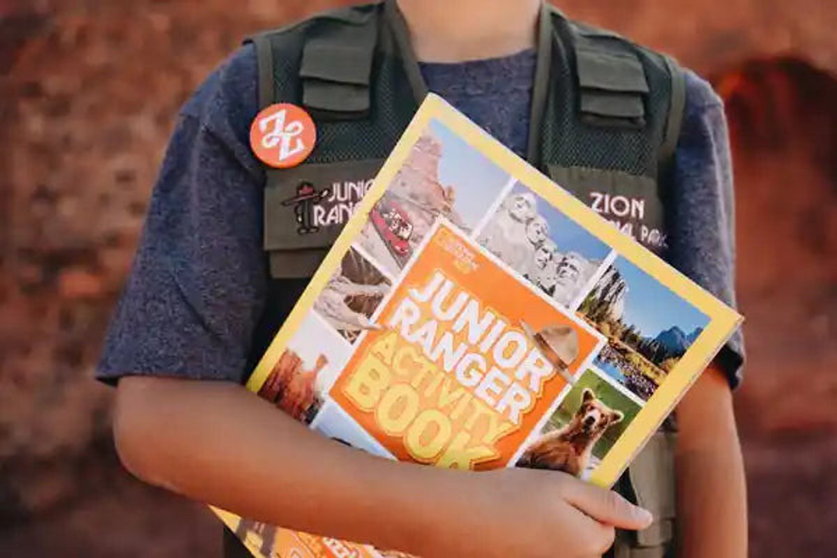 Young person wearing junior ranger vest and holding activity book.