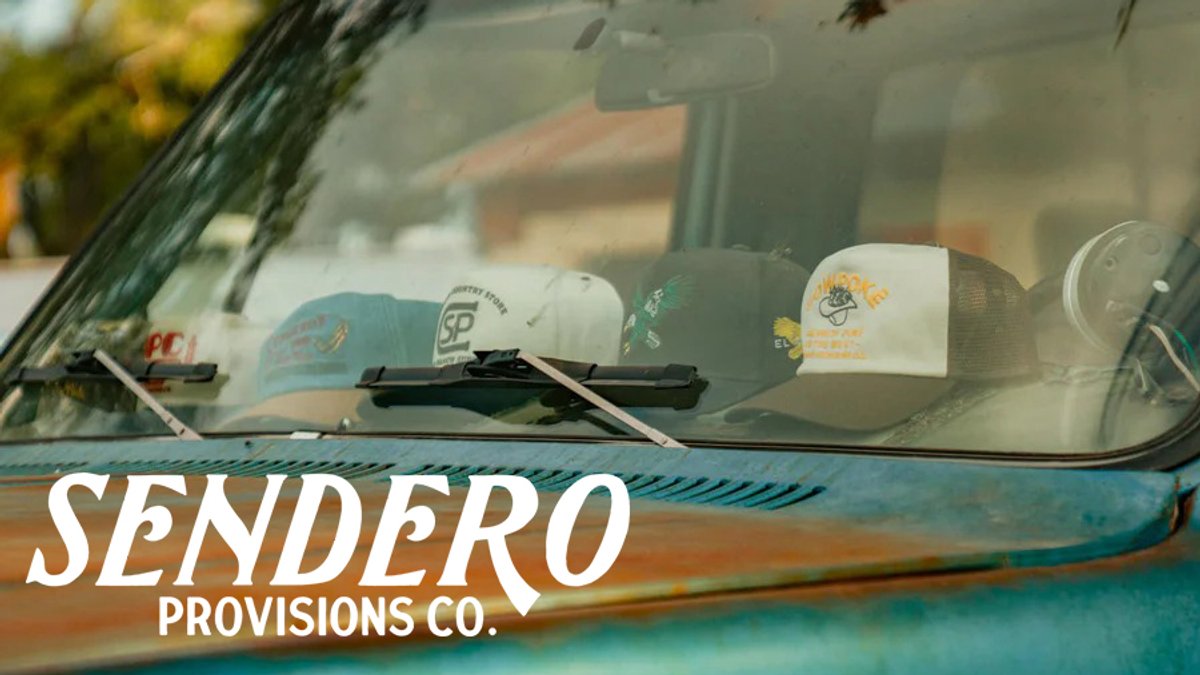 A row of various trucker hats is lined up inside the dashboard of a vintage turquoise truck under the Sendero Provisions Co. logo.