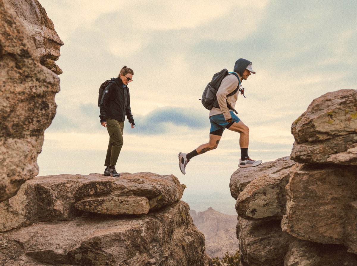 Two hikers walk on a rocky landscape. 