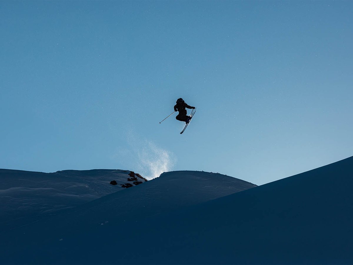 Skier silhouetted in the air doing a flip with ridge line below.