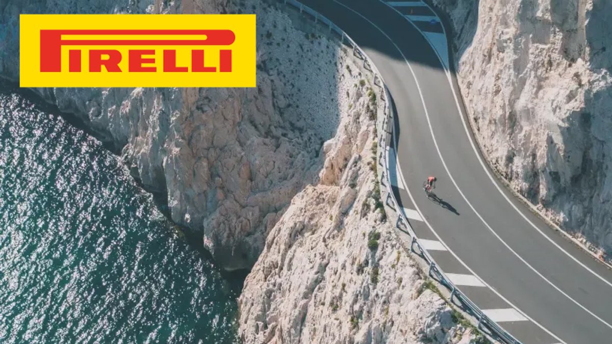 Pirelli tire brand logo displayed above an aerial view of a high-performance vehicle navigating a scenic coastal mountain road with steep cliffs and turquoise water below.