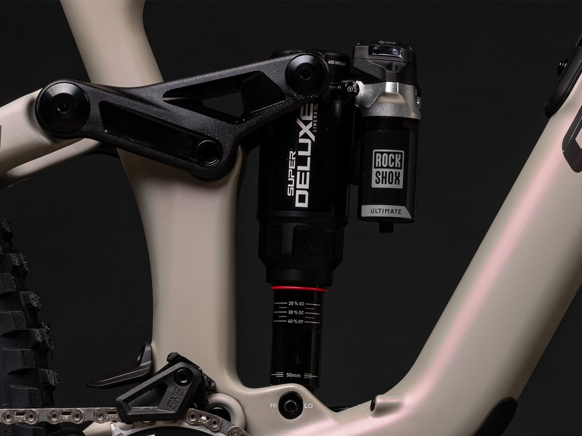Rear shock detail showing a RockShox Super Deluxe Ultimate with AXS wireless reservoir, mounted to the tan frame's rocker link.