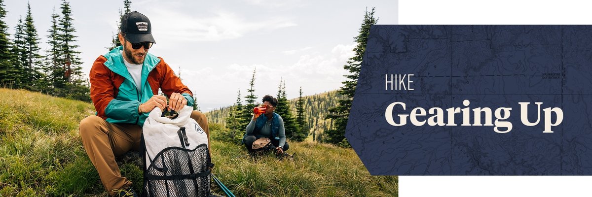 Two people sit in a grassy field. One is looking through his backpacking pack. The words, “hike gearing up” appear next to them.