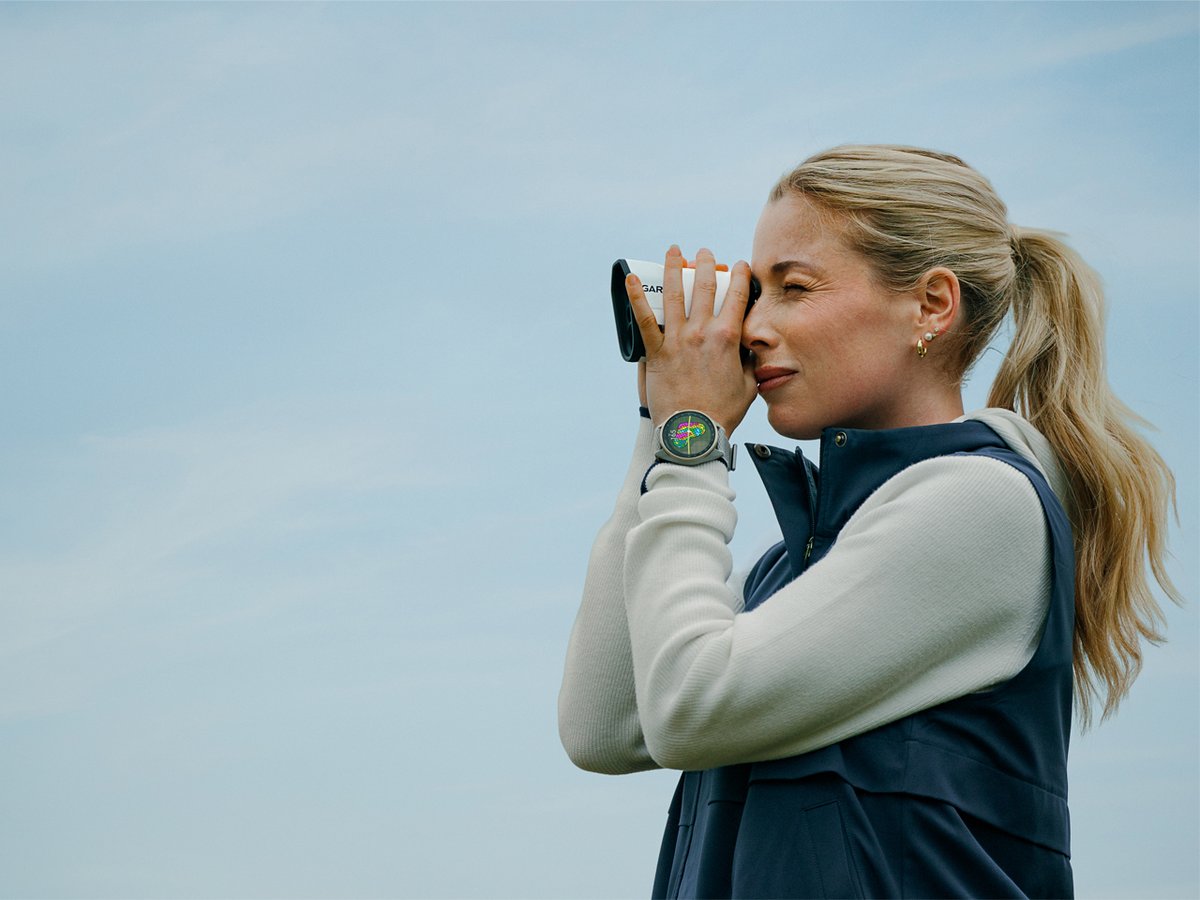 A woman uses a golf rangefinder while wearing a Garmin Approach S72 on her wrist.