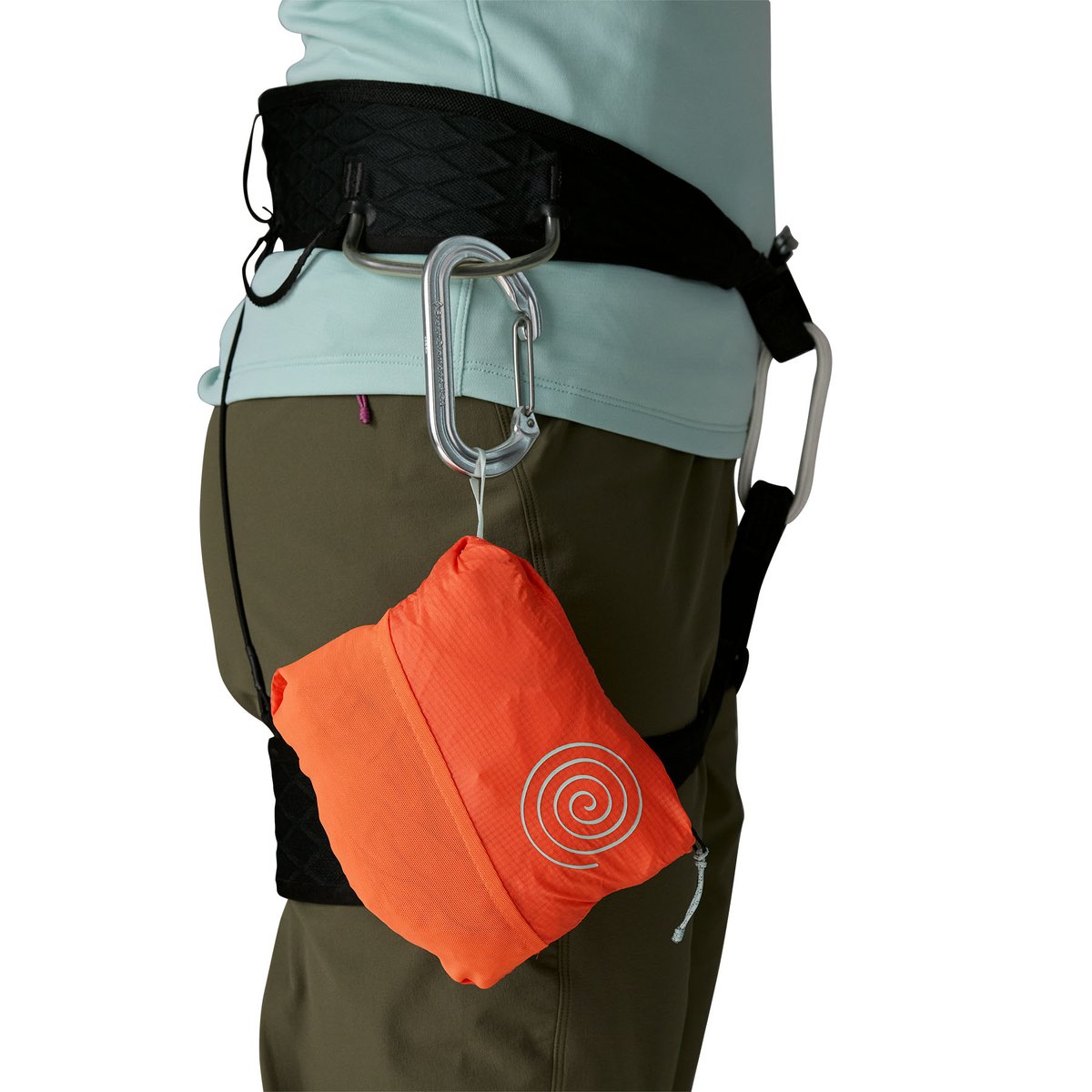Person wearing a climbing harness with the Houdini Rock Jacket packed into its stuff pocket and clipped to the harness.