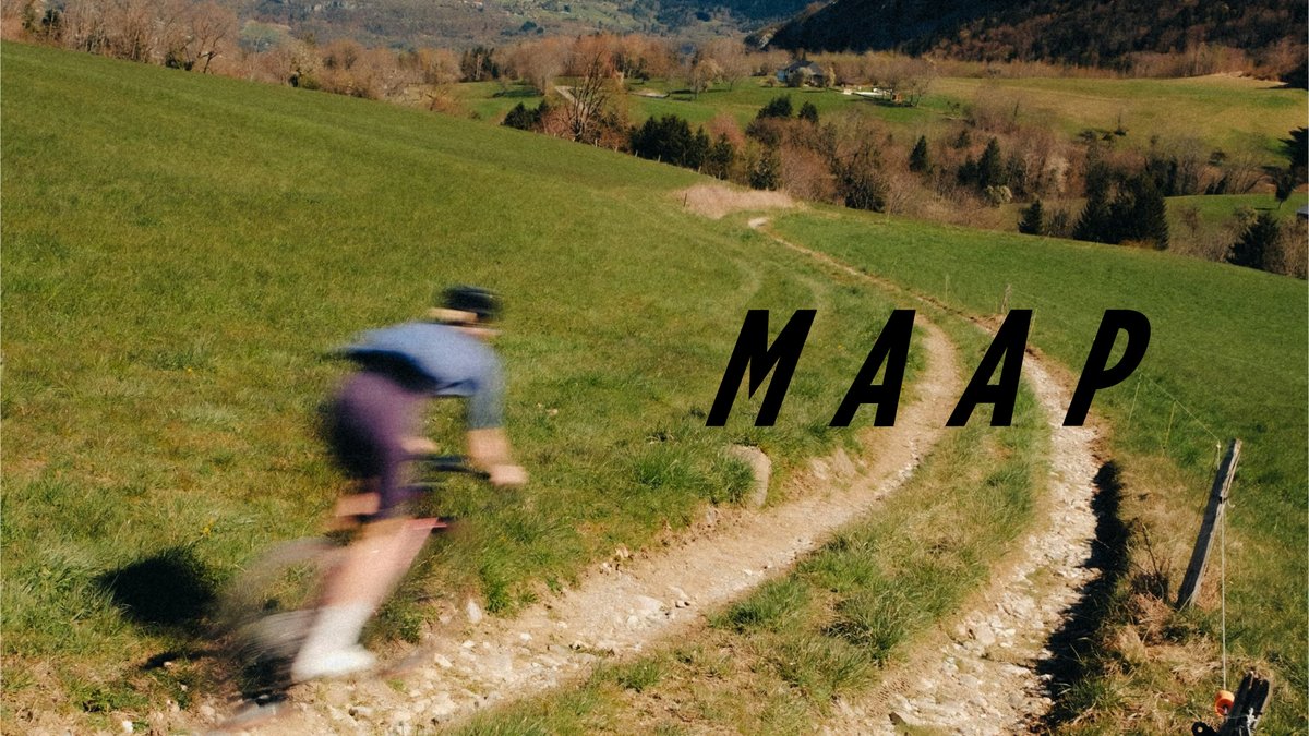 Mountain biker riding a rocky trail through rolling green hills with forested valley landscape in the background.