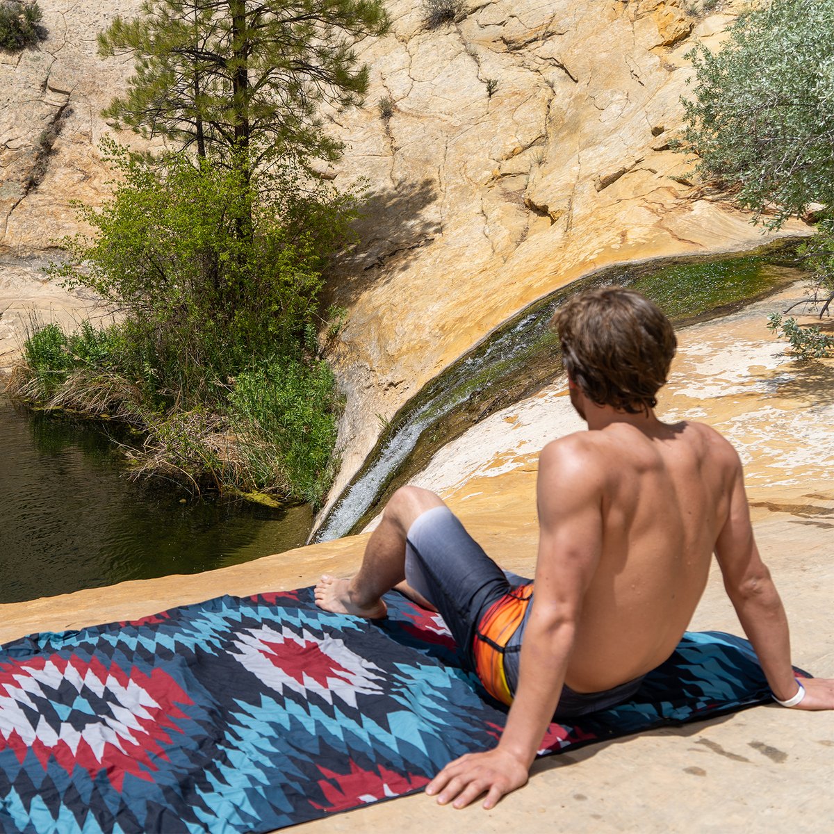 Peson sitting on Coalatree Kachula blanket on rocky waterfall overlook.