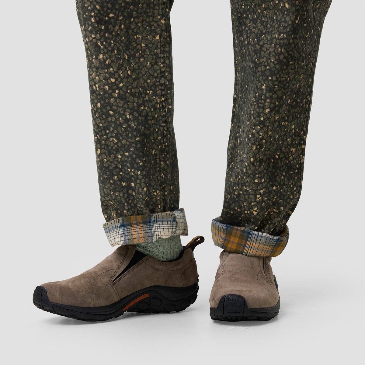 Person wearing olive speckled pants with plaid flannel cuff detail and taupe suede slip-on hiking boots with black soles.