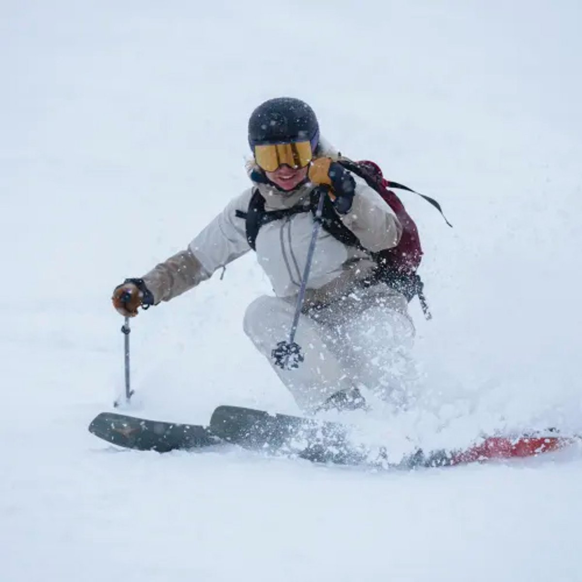 A skier in winter gear descends a snowy slope wearing a blue helmet, yellow goggles, and gray jacket while carving through fresh powder snow.