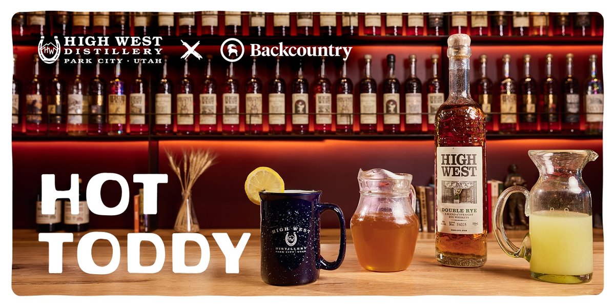 A bar countertop displays a mug with a lemon wheel, a glass pitcher of honey syrup, a bottle of High West Double Rye, and a glass jug ginger juice, set against shelves filled with liquor bottles; large text reads "Hot toddy" below the High West Distillery and Backcountry logos.