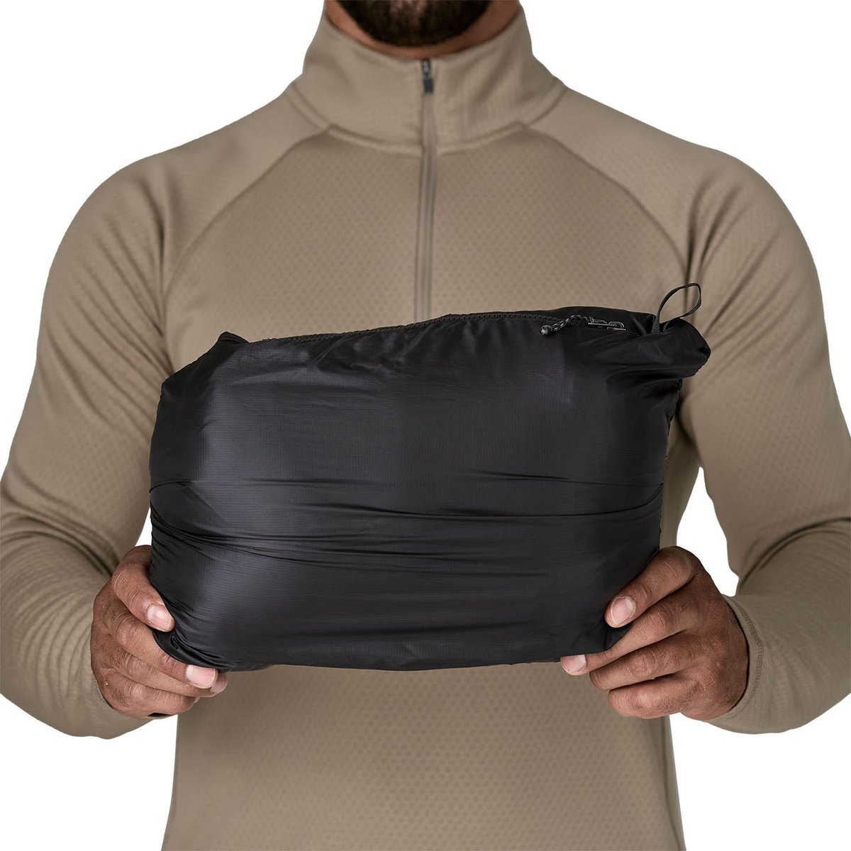 Person holding black Fitz Roy Down jacket that has been stuffed into pocket making compact oblong shape.
