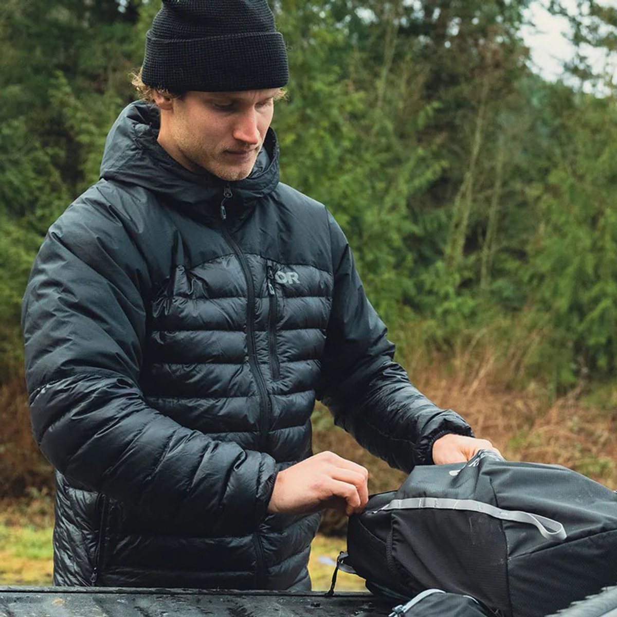 A man wearing a Men's Down Hoodie packs a backpack