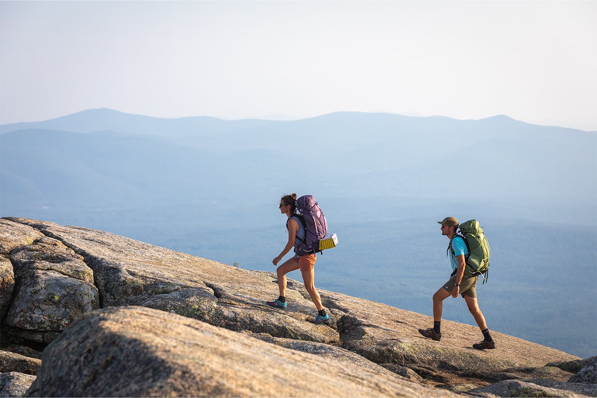 Two backpackers walk up a rocky incline.