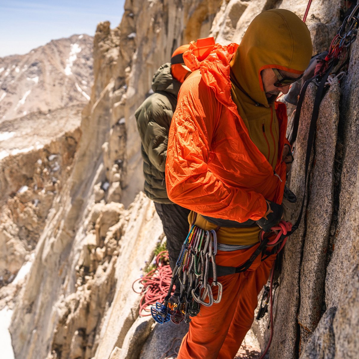 Climber on portaledge zipping up Houdini Rock Jacket over midlayers.